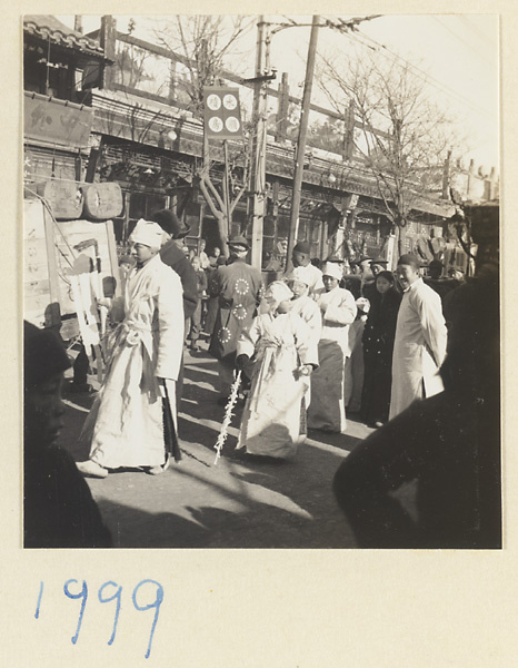 Mourners dressed in white carrying a soul banner and a staff in a simple funeral procession