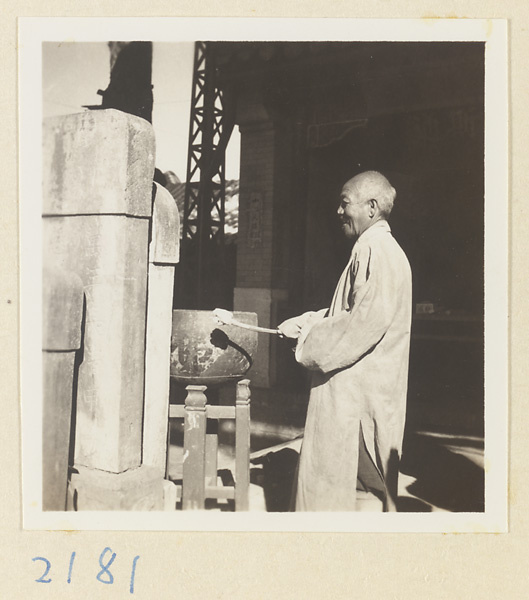 Monk striking an inscribed metal bell with a clapper on Miaofeng Mountain