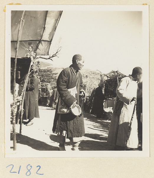 Monk with rosary and begging bowl passing vendors' stands on Miaofeng Mountain