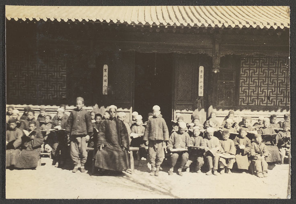 Ahung and schoolboys with books seated in front of building