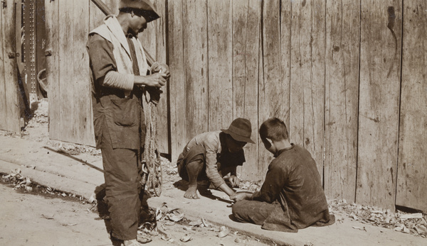 A man watching two children playing a game with stones, Hong Kong