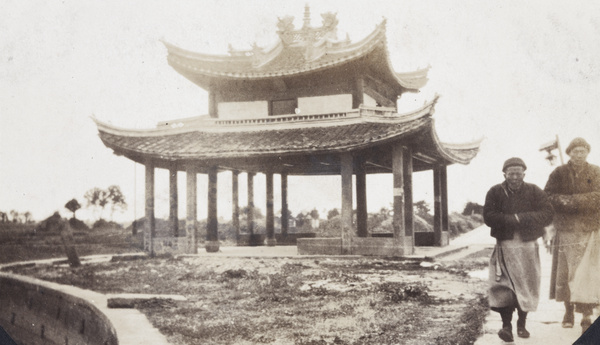 Two monks walking past a pavilion and grave mounds