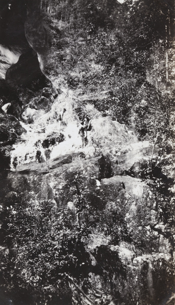 Three men wearing bathing costumes on a rocky ledge of a waterfall