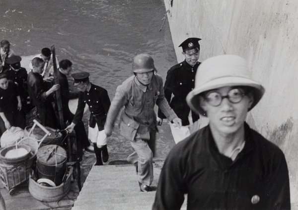 A Chinese soldier and Shanghai policemen unloading containers (likely food) from a boat, Shanghai, 1937