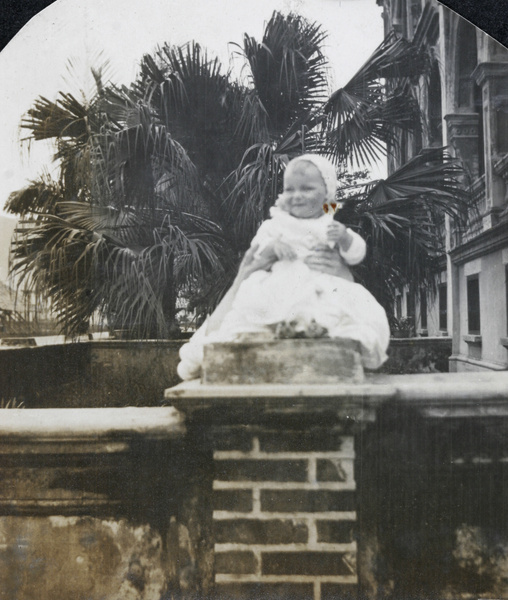 Gerald Johns in christening gown, posed on garden wall