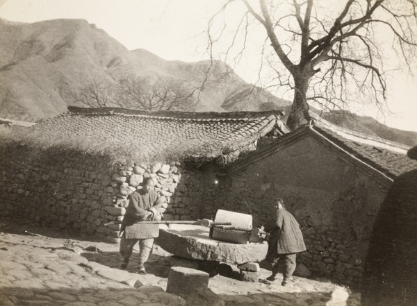 Two women with bound feet turning a millstone, near Beijing