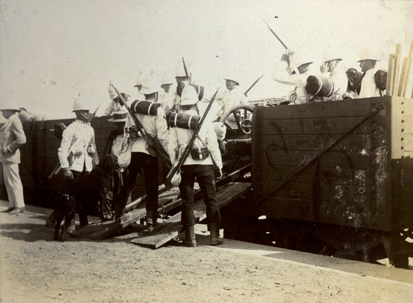 British soldiers and a gun on a train at a railway station