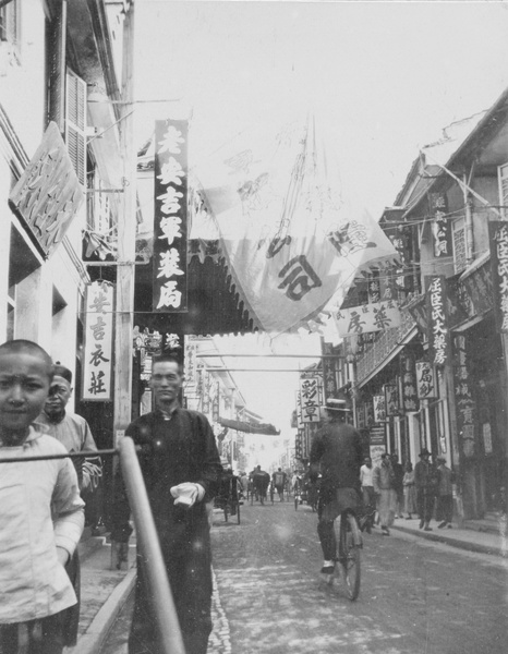 Shopping street, including three pharmacies. Boater hatted cyclist.