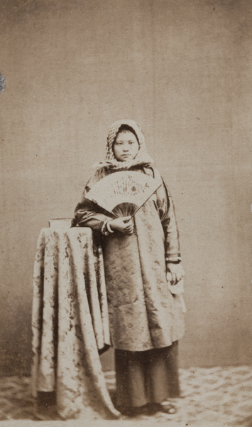 Portrait of a woman wearing a headscarf, with a fan and a book