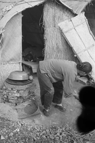 Woman sweeping and child sleeping in temporary shelter, Shanghai