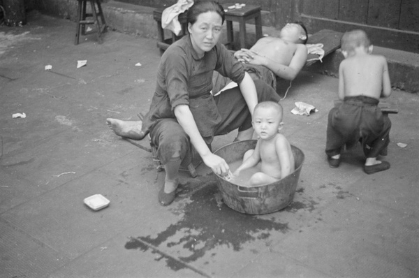 Mother bathing child in tin basin in street, Shanghai