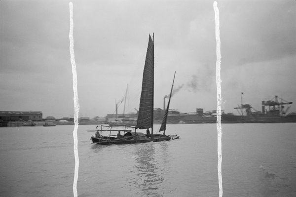 Junk sailing past wharfside cranes, Shanghai