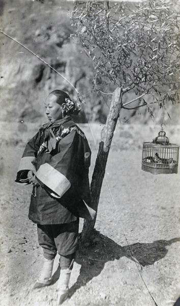 A woman with bound feet beside a bird cage