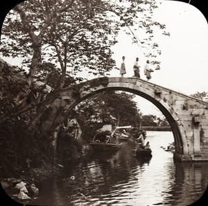 Three people crossing an old single arch bridge