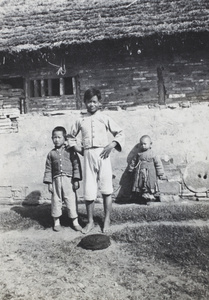 Children standing beside fresh dung and a thatched roof building
