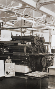 A print worker holding up a smallpox vaccination poster beside a large printing machine, Shanghai