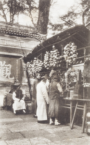Customers at a temple stall selling earthenware tea cups, prayer beads, incense and other offerings