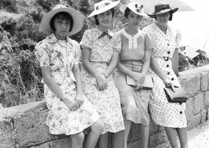 Gladys and Bea Hutchinson on a day trip with Elise Markham and Lilian Thoresen, sitting on a wall overlooking Castle Peak Road beac huts, Hong Kong