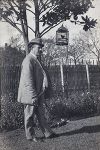 Mr Belyea standing near a birdcage hanging from a garden tree, 35 Tongshan Road, Hongkou,Shanghai