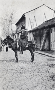 Young woman sitting side-saddle on a donkey standin in a cobbled street, Shanghai