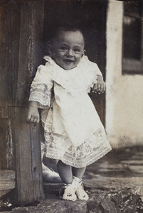 Sonny Hutchinson, wearing a lace baby gown, being lifted to stand on a summer house verandah, Moganshan