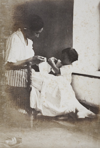 Sarah and Bea Hutchinson with pieces of fabric, beside the window of a summer house, Moganshan