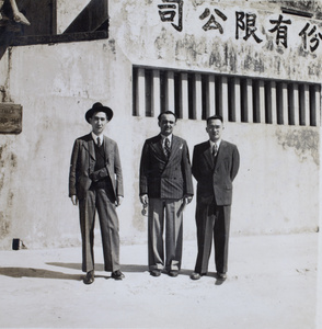 Tom Hutchinson, camera case around his neck, standing in a street with two unidentified men, Hong Kong