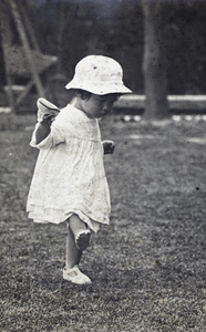 Bea Hutchinson, one shoe in hand and one shoe on her foot, walking across the garden grass, 35 Tongshan Road, Hongkou, Shanghai