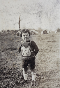 Unidentified boy wearing a hand knitted sweater, decorated with a squirrel pattern, and shorts, standing in a park with canvas tents, Shanghai
