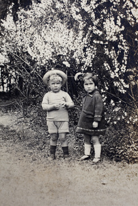 Unidentified boy and girl standing in front of a blooming bush, Shanghai