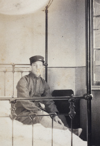 John Piry wearing a military uniform, on an iron-framed bed, 35 Tongshan Road, Hongkou, Shanghai