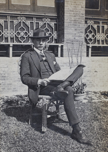 Bill Hutchinson wearing a pin-stripe suit and reading a newspaper in the garden, 35 Tongshan Road, Hongkou, Shanghai