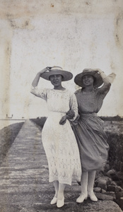 Nellie Thomas with her cousin, Sarah Penney, holding on to their hats while standing on an embankment wall, Wusong, May 1922