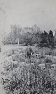 Fred Hutchinson, with a camera box and tripod, standing on stepping stones in a park, Shanghai