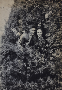 Unidentified man and woman posing in an evergreen shrub, Kunshan