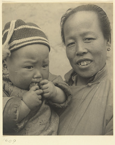 Woman wearing earrings and holding a child wearing a knitted cap