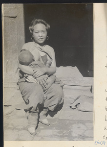 Woman with bound feet wearing earrings nursing a child in the Lost Tribe country