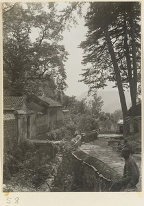 Man sitting on a wall next to temple buildings at Tan zhe si