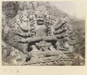 Relief of a multi-armed and multi-headed Bodhisattva holding a sceptre and wearing headdress and necklace made of skulls carved into the hillside at Yuquan Hill