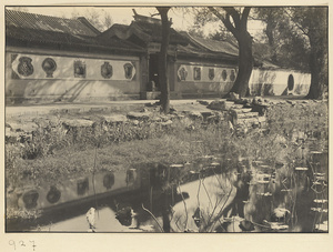 Gate and flanking walls with ornamental window shapes and a moon gate by the water at Nanhai Gong Yuan