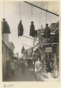 Street scene showing shop signs for a hemp-worker's shop (top), a tobacco pipe shop (right), and a tricycle