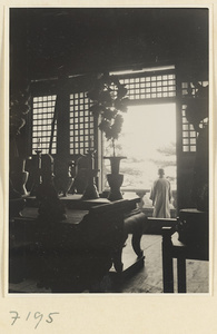 View from inside a temple building at Jie tai si showing altar with ritual objects, lattice windows, and a monk outside on a terrace