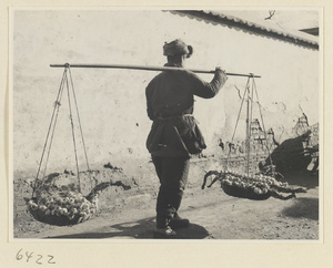 Garlic vendor with baskets of braided garlic hanging from a shoulder pole