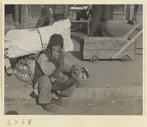 Small wheeled cart passing person sitting curbside with baskets