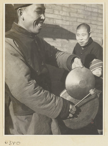 Puppeteer with two gongs called tang luo (smaller) and luo (larger) attracting an audience