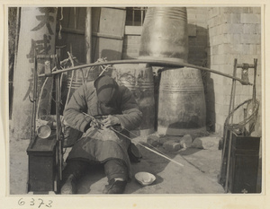 Itinerant ceramic repairman at work next to toolbox and gong called a tang or xiao lu jiang