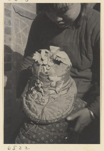 Woman holding child wearing a hat with appliqué work