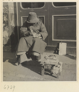 Street vendor sitting and writing next to wares and sign