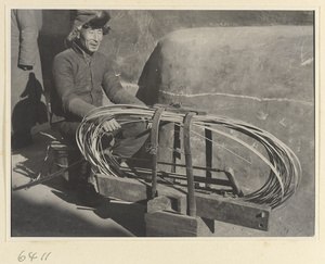 Mat mender seated next to box of tools and reeds