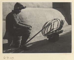 Mat mender seated next to box of tools and reeds